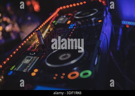 Rom, italien 9. januar 2025: Professioneller dj-Controller und Mixer, der in roten und blauen Lichtern bei einer lebhaften Club-Performance leuchtet, während die Menge zu Electr tanzt Stockfoto