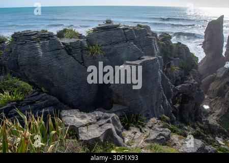 Eine zerklüftete Küste mit einzigartigen Felsformationen und üppiger grüner Vegetation. Die Meereswellen krachen gegen die Felsen und schaffen eine dramatische Meereslandschaft Stockfoto