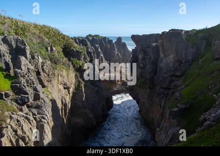 Eine atemberaubende Küstenlandschaft mit zerklüfteten Klippen und einem schmalen Wasserkanal. Die Szene wird durch helles Sonnenlicht beleuchtet, mit Stockfoto