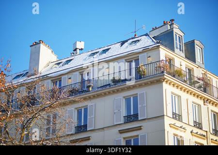 Traditionelles Apartmentgebäude im Haussmann-Stil in Paris mit Fensterläden, Balkonen mit Pflanzen und schneebedecktem Dach unter klarem blauem Himmel Stockfoto