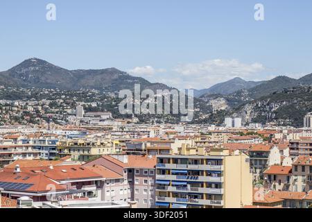 Blick auf Terrakotta-Dächer und Pastellgebäude, die sich unter klarem Himmel in Richtung entfernter, majestätischer Berge stürzen, Nizza, Frankreich. Stockfoto