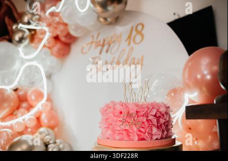 Eleganter rosafarbener Geburtstagskuchen mit Rüschen und Kerzen, gestaltet für eine 18. Geburtstagsparty mit weichen Ballons und festlicher Einrichtung. Stockfoto