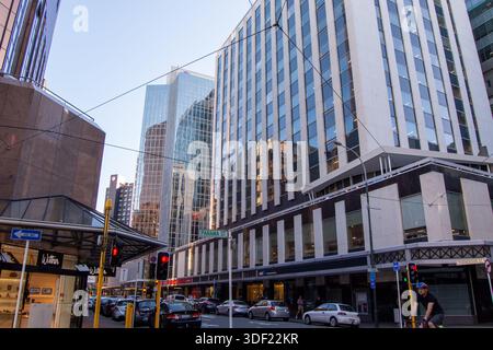 Eine geschäftige urbane Straßenszene mit modernen Wolkenkratzern und einer geschäftigen Kreuzung. Die Gebäude reflektieren Sonnenlicht und zeigen Glasfassaden. Verkehr Stockfoto