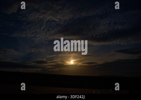 Ein ruhiger Nachthimmel, beleuchtet von einem hellen Vollmond, umgeben von schroffen Wolken und sanften Lichtstrahlen. Die Szene weckt ein Gefühl von Ruhe und Ruhe Stockfoto