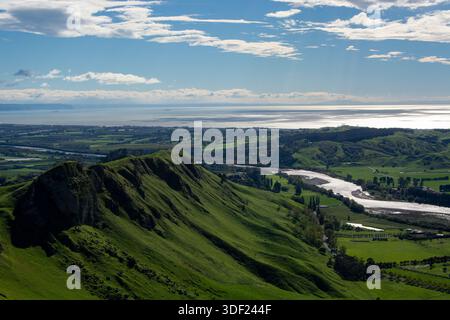 Ein Panoramablick auf üppig grüne Hügel und Täler unter einem hellblauen Himmel mit verstreuten Wolken. Ein sich windender Fluss fließt durch die Landschaft, reflektierend Stockfoto