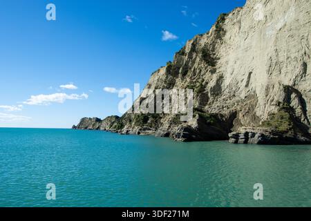 Ein atemberaubender Blick auf die Küste mit steilen Klippen, die sich über einem türkisfarbenen Meer unter einem klaren blauen Himmel erheben. Die felsige Küste verleiht dem ruhigen lan noch mehr Textur Stockfoto