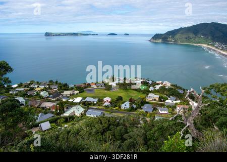 Aus der Vogelperspektive auf eine Küstenstadt mit Häusern inmitten üppiger Vegetation, mit Blick auf ein ruhiges Meer und ferne Inseln unter teilweise bewölktem Himmel. Stockfoto