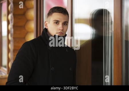 Jungen gutaussehenden Mann in der klassischen schwarzen Mantel stehen am Fenster Stockfoto