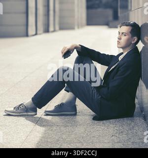 Young Fashion Business Mann mit einem Mobiltelefon an der Wand saß Stockfoto