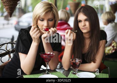 Zwei junge Frauen essen eine Dessert im Straßencafé Stockfoto