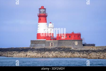 Longstone Lighthouse auf den Farne Islands in Northumberland, England, mit seinem roten Turm, der vor einem weichen blauen Himmel steht. Stockfoto