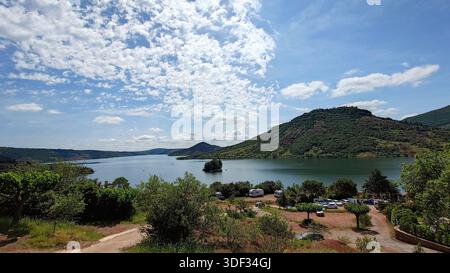 26. Mai 2024, Celles, Frankreich: Blick auf den Salagou-See vom Campingplatz Le Mas de Riri. Camper und üppige Hügel unter einem dramatischen blauen Himmel mit weißen Wolken. Stockfoto