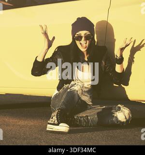 Wütend mode Hippie Frau in Schwarz Leder Jacke sitzen auf Bürgersteig neben ihrem Auto Stockfoto