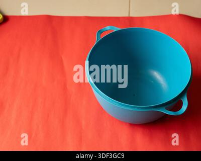 Leere blaue Schüssel auf rotem Hintergrund, präsentiert als auffälliges Modell für Küchenutensilien mit Farbkontrasten und Kopierraum. Stockfoto