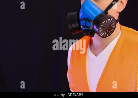Profilaufnahme einer Person in Sicherheitsweste mit blauer Atemschutzmaske vor dunklem Hintergrund Stockfoto