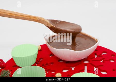 Schokoladenglasur in der Schüssel mit Holzlöffel und Silikon-Backbecher auf dem Tisch Stockfoto
