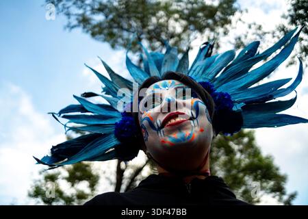 Niedrigwinkelporträt eines Teilnehmers mit Schädel-Make-up und blauem Kopfschmuck während der Day of the Dead Parade in Mexico City, Mexiko. Stockfoto