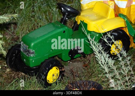 Verwitterter grüner und gelber Aufsitzspielzeugtraktor in Garteneinstellung Stockfoto