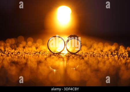 Romantische Silhouette goldener Eheringe bei Sonnenuntergang, symbolisiert Liebe und ewiges Engagement. Kontrastreiche goldene Stunde-Fotografie Stockfoto