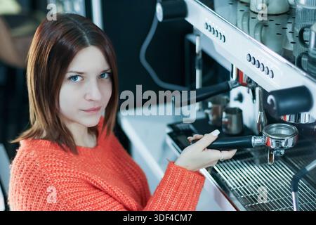 Der Barista in einem gemütlichen Strickpullover bereitet Kaffee mit Portafilter in Café-Umgebung sorgfältig zu Stockfoto
