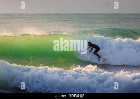 Surfer im Taucheranzug reitet auf der Welle im kalten Wintermeer mit Abendsonne Stockfoto