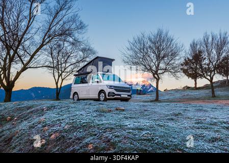 Wohnmobil parkt in der Natur an einem Wintermorgen mit gefrorenem Boden und schneebedeckten Berggipfeln Stockfoto