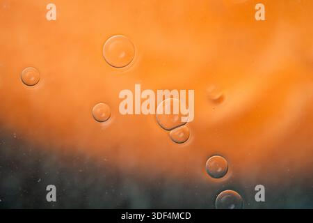 Makrofotografie mit leuchtend orangefarbener, flüssiger Textur mit verstreuten Blasen, perfekt für abstrakte künstlerische Hintergründe. Stockfoto