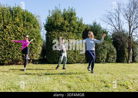 Weitwinkelansicht von drei Personen, die an einem sonnigen Tag gemeinsam im Park trainieren Stockfoto