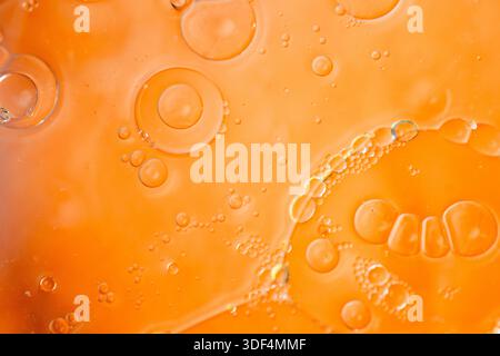 Makrofotografie mit leuchtend orangefarbener, flüssiger Textur mit verstreuten Blasen, perfekt für abstrakte künstlerische Hintergründe. Stockfoto