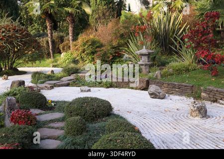 Traditioneller japanischer Zen-Garten mit Steinlaternen, geharktem Kies wirbelt um Felsen, immergrünen Sträuchern, bunten Herbstahorn und üppigem Grün Stockfoto