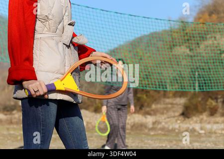 Partielle Ansicht einer Frau in rotem Ärmel, die mit gelbem Schläger auf dem Platz im Freien mit Spielern aus der Ferne greift. Stockfoto