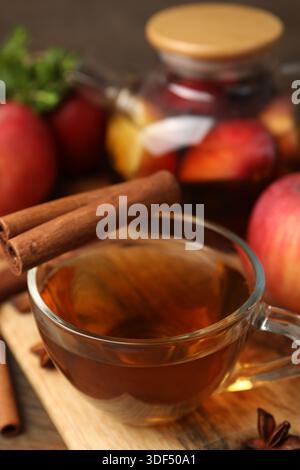 Aromatischer Früchtetee in Glasbecher, Teekanne, Äpfel, Minze und Gewürze auf dem Tisch, Nahaufnahme Stockfoto
