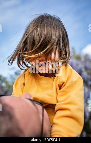 Niedriger Blickwinkel eines glücklichen Kindes in gelbem Oberteil, der auf Papa in seinen Händen blickt Stockfoto