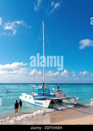 Ein Katamaran, der Touristen Segeltörns am Sandstrand von Waikiki Beach in Hawaii anbietet Stockfoto