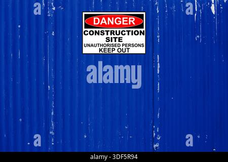 Halten Sie auf der Baustelle ein Schild auf einem alten Sperrzaun aus Wellblech, der mit blauem Hintergrund bemalt ist. Stockfoto