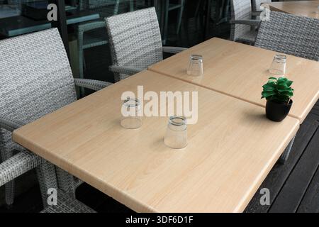 Essen im Freien mit einem Holztisch, Stühlen, Trinkgläsern und einer Topfpflanze Stockfoto