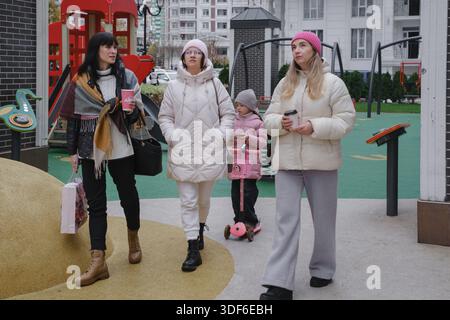 Freunde genießen Freizeit im Freien mit einem kleinen Kind in einem modernen Wohngebiet Spielplatz, Wintersaison, zeitgenössische städtische Wohnanlage Stockfoto