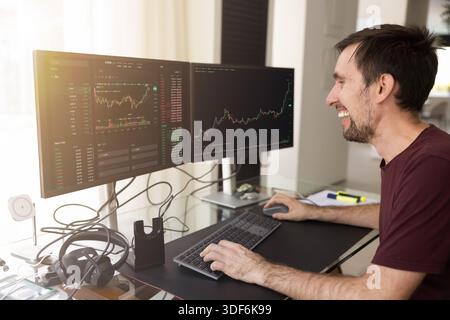 Glücklicher erfolgreicher Investorenmann, der Wachstumsdiagramme auf großen Monitoren analysiert Stockfoto