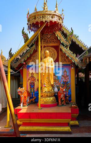 Goldene Mönchsstatue, bewacht von traditionellen Tigerskulpturen im Wat Phra That Doi Kham Tempel auf der Bergseite von Chiang Mai, Nordthailand Stockfoto
