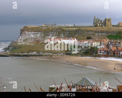 Whitby Harbour und Whitby Abbey im Winter mit Schneestäuben und wenigen Menschen am Strand, außerhalb der Saison, North Yorkshire, England, Großbritannien Stockfoto