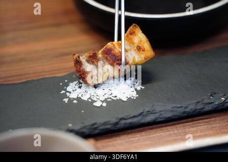 Knuspriger Schweinebauch mit grobem Meersalz auf einem schwarzen Schieferteller, Feinschmecker aus nächster Nähe Stockfoto