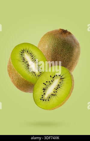 Köstliche Kiwi-Früchte, die in zwei Hälften geschnitten sind, mit saftigem, grünem Fruchtfleisch in der Luft schwimmen, Nahaufnahme auf grünem Hintergrund. Ausgezeichnet für Designmenü gesundes Vitamin foo Stockfoto