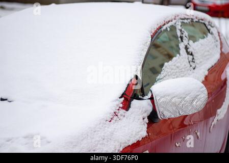 Ein abstraktes Nahfoto eines roten metallischen Autoteils (möglicherweise ein Seitenspiegel oder eine Tür), bedeckt mit weißem Schnee und Frost. Stockfoto