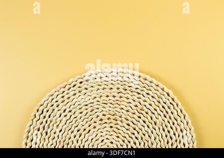 Draufsicht der braunen Korbplatte auf gelbem Hintergrund. Rundes Strohfach, flache Ladefläche, Kopierraum. Stockfoto