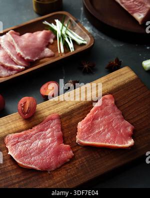 Geschnittenes rohes Rindfleisch-Steaks auf hölzernem Schneidebrett mit Gewürzen und Kirschtomaten auf dunklem Tisch Stockfoto
