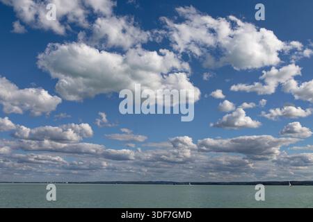 Ein malerischer Blick auf einen hellblauen Himmel voller geschwollener weißer Wolken mit Blick auf ein ruhiges Gewässer. Stockfoto