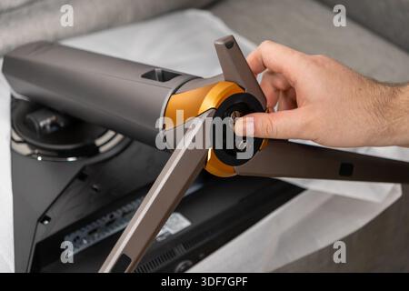 Nahaufnahme einer Hand, die einen eleganten, grau-goldenen Monitorständer auf einem schwarzen Bildschirm installiert hat und die neue elektronische Hardware aus dem Auspacken und Einrichten hervorhebt Stockfoto