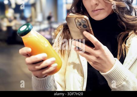 Eine Frau scannt den Barcode auf einer Joghurtverpackung in einem Supermarkt oder Lebensmittelgeschäft mit ihrem Smartphone. Qualität und Frische der Produkte Stockfoto