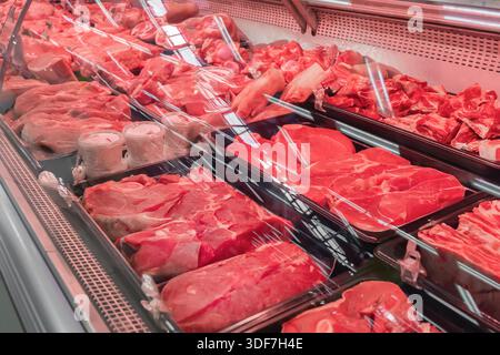 Fleisch wird in einem Geschäft mit rotem Rindfleisch und Schweinefleisch serviert. Verschiedene Fleischstücke sind für die Kunden sichtbar. Die Umgebung ist ein Fleischteil in einem Supermarkt Stockfoto