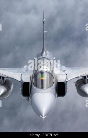 Luft-Luft-Foto der tschechischen Luftwaffe Saab JAS 39C Gripen während des Fluges an den NATO Days 2025. Das Bild zeigt eine Nahansicht des Piloten im Cockpit und zeigt die Standardflugausrüstung. Der Gripen ist ein einmotoriger Mehrzweckjäger mit Delta-Flügel und Vorwärtskantflügeln. Er wird von einem General Electric F414G Turbofan-Motor angetrieben und dient in der Luftverteidigung und NATO-Interoperabilität, wobei er die Bedingungen während des Fluges und die Details des Flugzeugdesigns während einer Veranstaltung in der öffentlichen Luftfahrt hervorhebt. Stockfoto